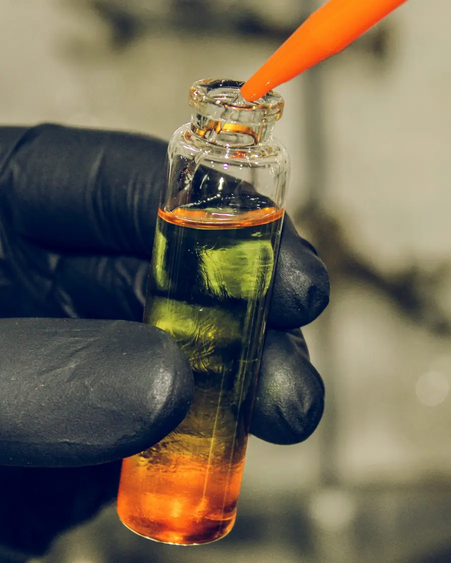 A gloved hand adding reagent drops to a water-sample vial during a chemistry test