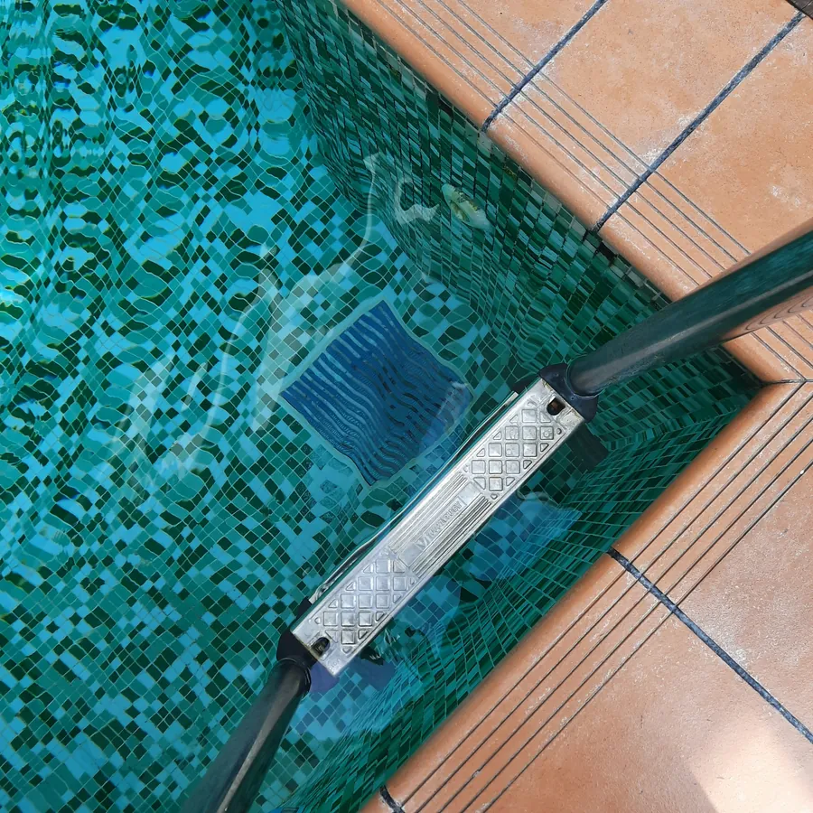 Looking down at a pool vacuum head on green mosaic tile beside terracotta coping
